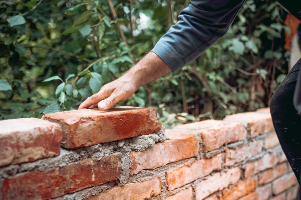 mason worker building with bricks, mortar, trowel. Industrial construction site details.