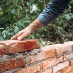 mason worker building with bricks, mortar, trowel. Industrial construction site details.